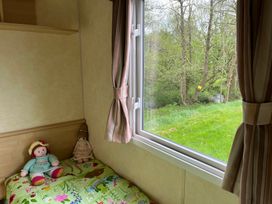 A bedroom with dolls on a bed and a view of trees at Sylvan in Builth Wells