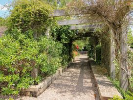 A garden pathway with a wooden trellis and surrounding greenery at Uplands Cottage in Ledbury