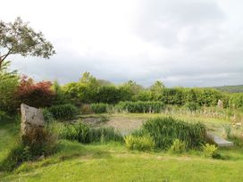 A garden with a pond, shrubs, and grass at The Dovecote in Fishguard