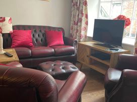 A living room with a sofa, armchair, and tv at The Bittern in Blakeney, Norfolk