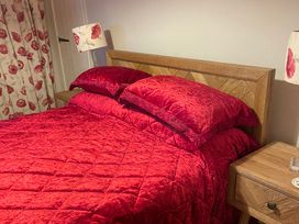 A bed with red bedding and pillows and a side table with a lamp at The Bittern in Blakeney, Norfolk