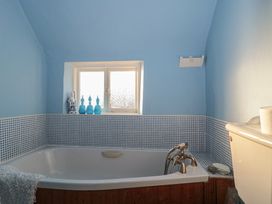 A bathroom with a bathtub and window at Vine Cottage in Alderton
