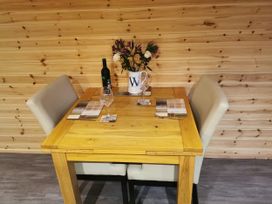 A dining table with a wine bottle and flowers at Lodge 2 Pontyates