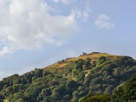 A hill with trees and ruins under a cloudy sky at Woodpecker Cottage, Llangollen