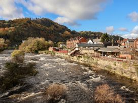 A view of a river and buildings by the hills at Woodpecker Cottage in Llangollen