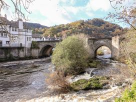 A bridge over a river with buildings and trees at Woodpecker Cottage in Llangollen