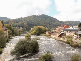 A river with buildings along the bank and mountains in the background at Owl Cottage in Llangollen