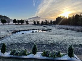 A pond with grass and trees during sunrise at Crofters Suite