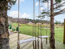 A swing hanging from a tree with a view of a grassy field and trees at Crofters Suite