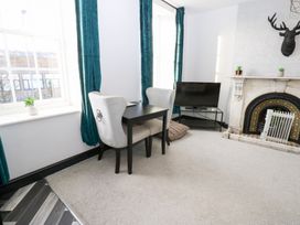 A living room with a table and chair beside a fireplace at Lowther Apartment in Whitehaven