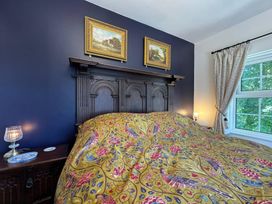 A bedroom with a bed, nightstand, lamp, and pictures at St. James Cottage, Liskeard