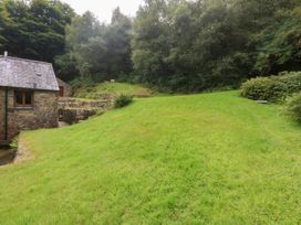 A stone building with a slate roof next to grass and trees at Ty Newydd in Llanrhychwyn near Llanrwst