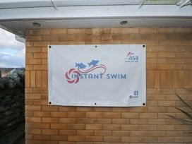 A banner displaying 'INSTANT SWIM' on a brick wall at King Arthur Suite Trearddur Bay