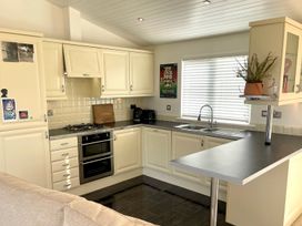 A kitchen with cabinets, stove, and sink at Lowena Lodge Whitsand Bay Holiday Park near Millbrook
