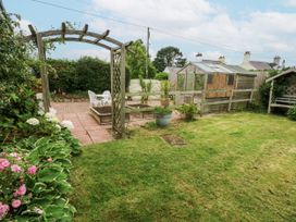 A garden with a greenhouse and seating area at 1 Maes Y Ffynnon in Llandegfan