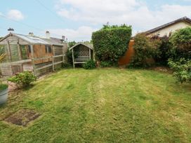 A garden with a greenhouse and wooden bench at 1 Maes Y Ffynnon Llandegfan