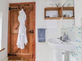 A bathroom with a sink, towel, bathrobe, shelf and wooden door at The Hayloft in Bodelwyddan