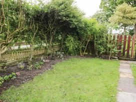 A garden with trees, a fence, a flower bed, and grass at Billy's Cottage in Maryport
