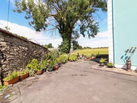 An outdoor area with a stone wall, potted plants, tree, and pathway at Ash House Ballyvaughan