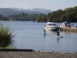 Two paddleboarders on the water with boats and mountains in the background at School Cottage, Troutbeck Bridge near Windermere