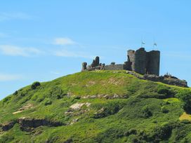 A castle on a hillside with flags at Gowan Brae in Criccieth