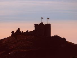 A castle on a hilltop with flags at Gowan Brae in Criccieth