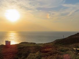 A seaside view with a sun setting over the ocean and a lighthouse at Penrhos Walks in Holyhead