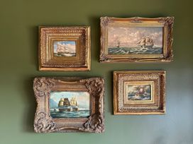 Four framed paintings of ships on a green wall at The Garden Cottage and Carriage House, Annagry, County Donegal