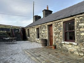 An outdoor view of a stone house with a table and barrel at Cobble Stone Cottage near Leabgarrow, County Donegal