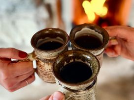 Three mugs with hot beverage held by hands near a fireplace