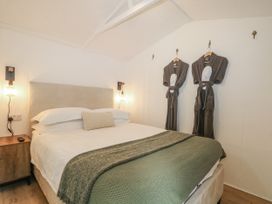 A bedroom with a bed and robes hanging on the wall at Charltons Hollow Cabin in Haywards Heath