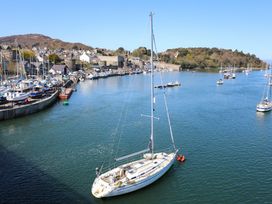A sailboat on water in a harbor with moored boats and land in the background at Ty Gelert in Conwy