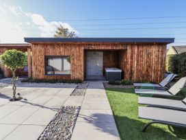 A wooden cabin with a hot tub and lounge chairs at Honeymug near Branton Powburn