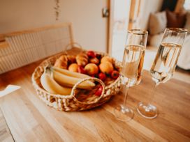 A kitchen with a basket of fruit and two glasses of sparkling wine at Driftwood in Carreglefn near Llanfechell