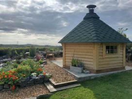 A log cabin in a garden with flowers and a gravel path at Rowan in Carreglefn near Llanfechell