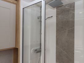 A shower with glass door and tiled wall at Maple Lodge Teigngrace near Kingsteignton