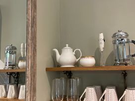 A kitchen shelf with a teapot, coffee press, milk frother, and drinking glasses at Garden Apartment in Par