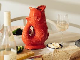 A dining table with a red fish-shaped carafe and a glass of wine at The Porthole in Newton Ferrers