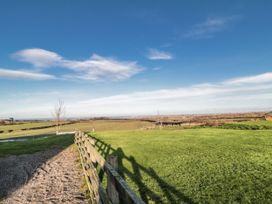 A grassy field with a wooden fence and trees at Wheelhouse Cottage