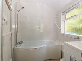 A bathroom featuring a bath tub with shower and sink at Seaview Hafod Y Graig in Morfa Bychan