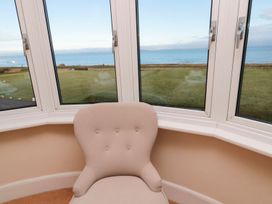 A snug room with a chair and bay windows overlooking the sea at Glen Avon in Seahouses