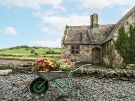A wheelbarrow with flowers in front of a stone building at Holy Trinity Cottage in Millom