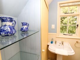 A bathroom with a white sink and blue pitchers on a glass shelf at Smugglers Cottage in New Milton