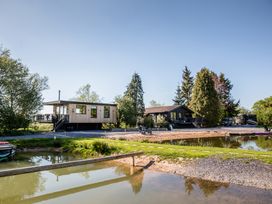 A wooden house with a pond and trees at The Larch House in Farndon