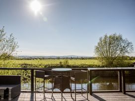 A deck with table and chairs overlooking fields and water at The Larch House in Farndon