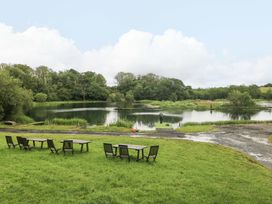 A lake with fishing area and wooden chairs at Oak Lodge Mynydd Cerrig near Porthyrhyd
