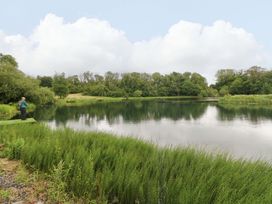 A lake with a fisherman and surrounding greenery at Oak Lodge Mynydd Cerrig near Porthyrhyd