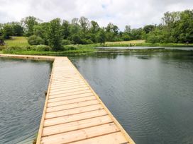 A wooden walkway over water with trees and grass at Ash Lodge in Mynydd Cerrig near Porthyrhyd