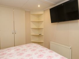 A bedroom with a bed, wardrobe, shelf, television, and radiator at The Chalet at Tyn Lon, Chwilog