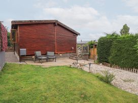 A wooden cabin with a patio area and chairs in the garden at Charnwood
